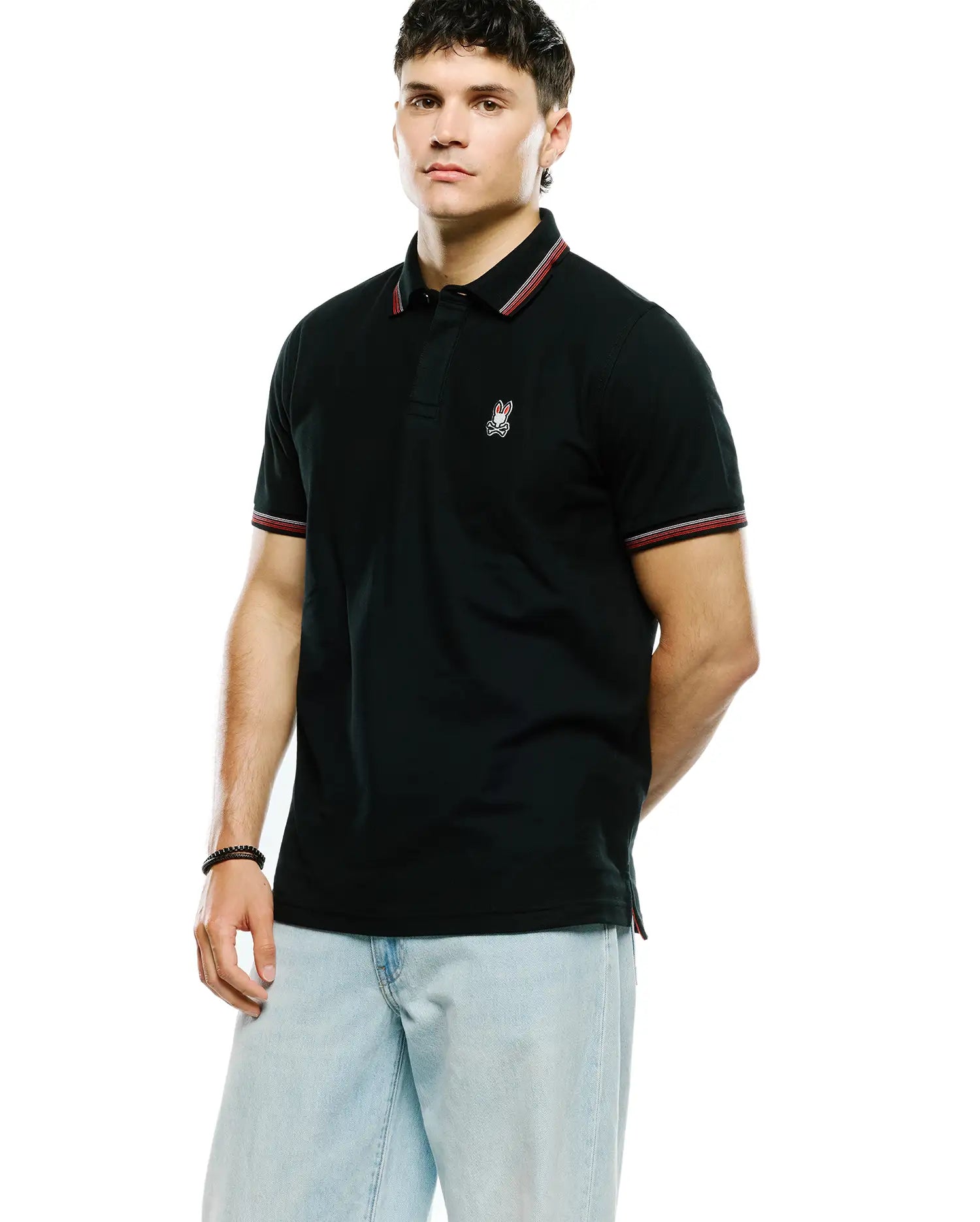 Mens Jaydon Pique Polo, black with classic fit, featuring a small embroidered Psycho Bunny skull logo on the left chest, and red and white tipping on the ribbed collar and sleeve cuffs.