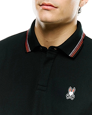 Black Mens Jaydon Pique Polo with classic fit, pique texture, and a small embroidered Psycho Bunny skull logo on the left chest. Collar features red and white stripe accents.