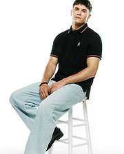 Mens Jaydon Pique Polo in black, featuring a classic fit, textured pique fabric, red and white striped collar and cuffs, and a small embroidered Psycho Bunny skull logo on the left chest.