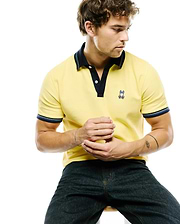 Mens Jaydon Pique Polo, classic fit, yellow pique with navy collar, placket, and striped cuffs. Features a small embroidered Psycho Bunny skull logo with blue ears on the left chest.