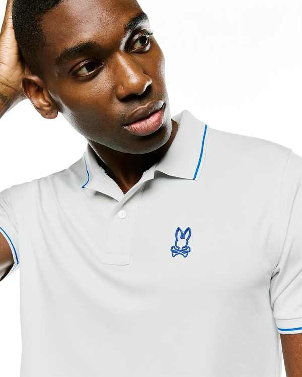 Men's Joji Performance Polo, light grey pique knit with a classic fit, features a two-button placket, blue tipping on the collar and sleeve cuffs, and an embroidered blue Psycho Bunny skull logo on the left chest.