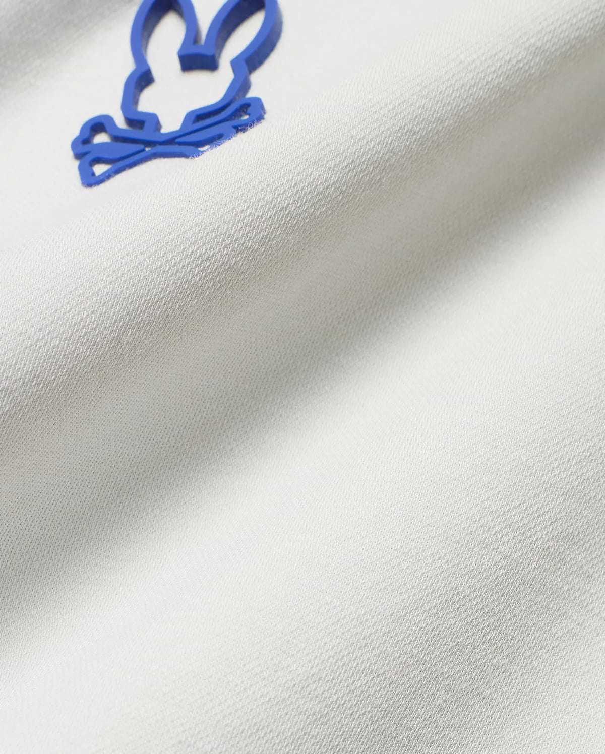 Men's Joji Performance Polo in crisp white, breathable pique knit fabric, showcasing the iconic, raised blue Psycho Bunny skull logo on the chest.