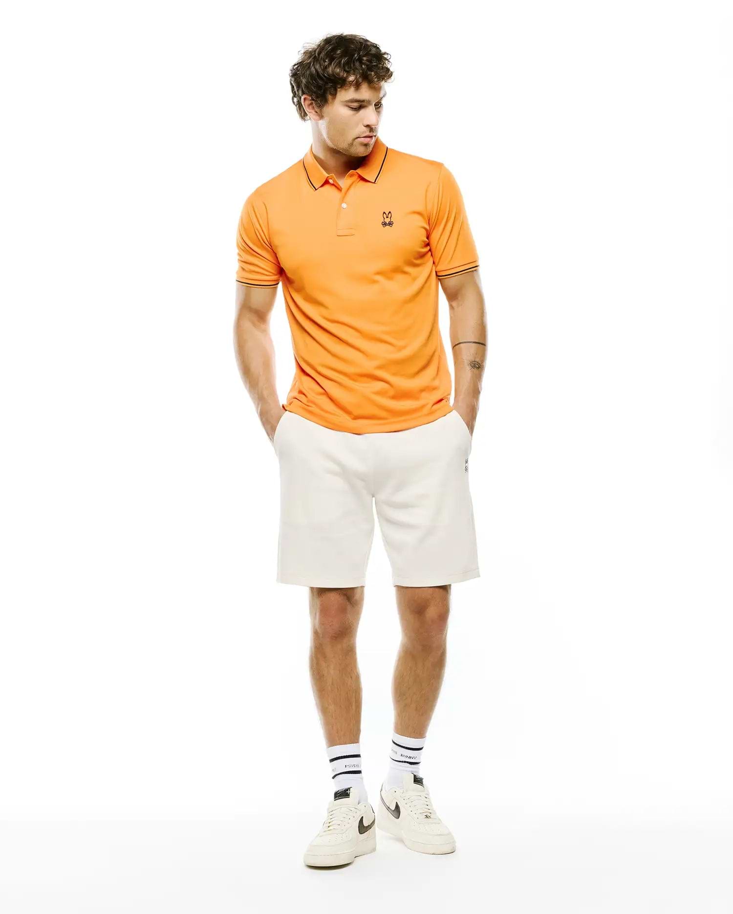 Mens Joji Performance Polo, vibrant orange slim fit pique polo with black trim on collar and cuffs, featuring a small embroidered Psycho Bunny skull logo on the left chest.