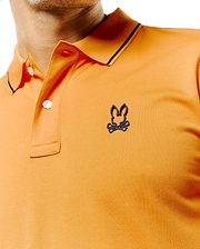Mens Joji Performance Polo, vibrant orange pique knit polo shirt with classic fit, featuring a dark grey raised Psycho Bunny skull logo on the left chest, black collar tipping, and white buttons.