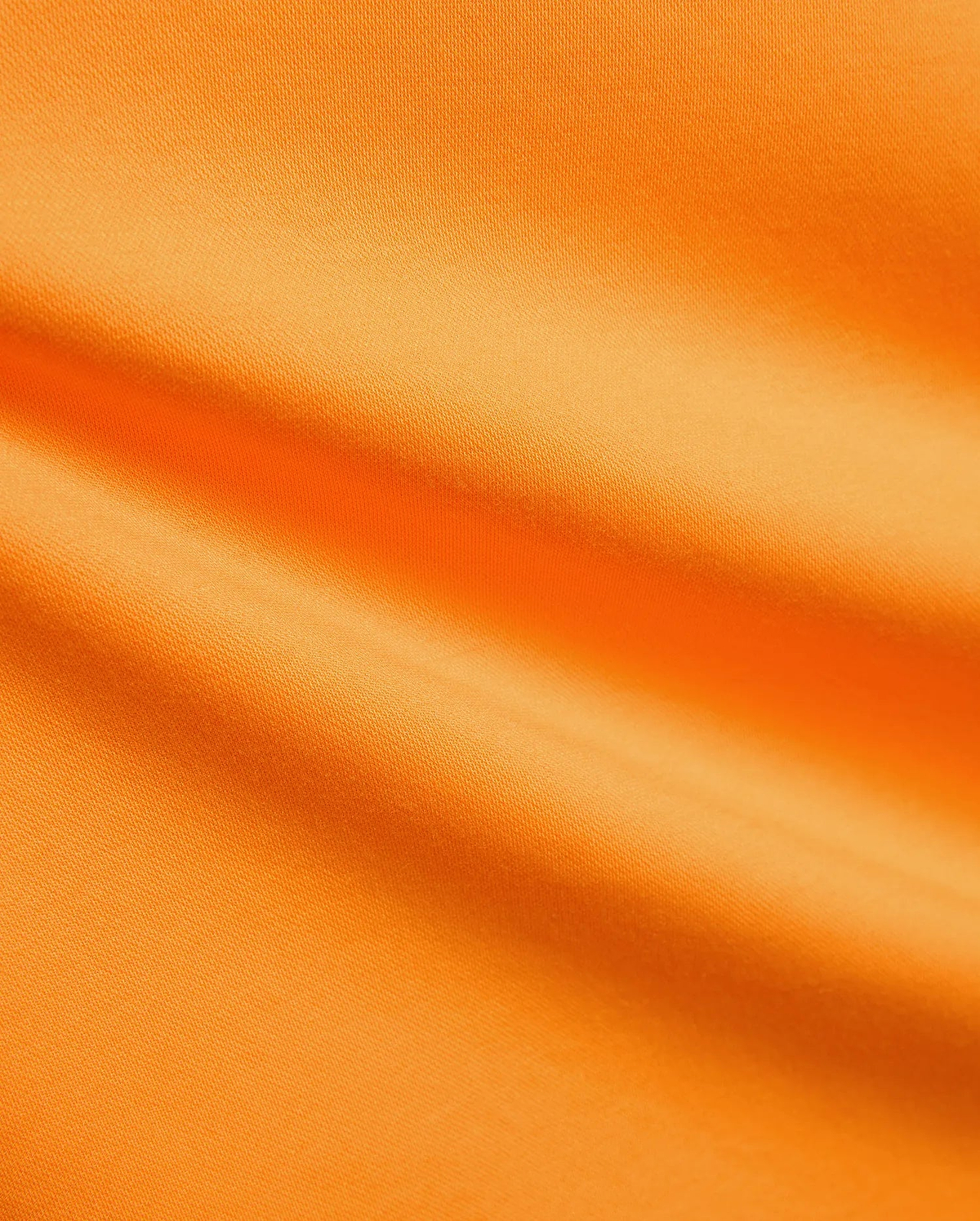 Mens Joji Performance Polo in a bright, energetic orange, featuring a finely textured, breathable pique knit fabric with subtle diagonal lines and soft folds, ideal for refined streetwear.
