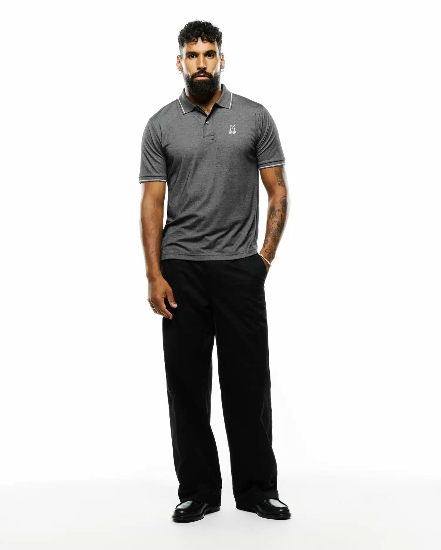 Mens Joji Performance Polo, dark grey heathered performance jersey with classic fit, white tipped collar and sleeve cuffs, two-button placket, and small embroidered white Psycho Bunny skull logo on left chest.