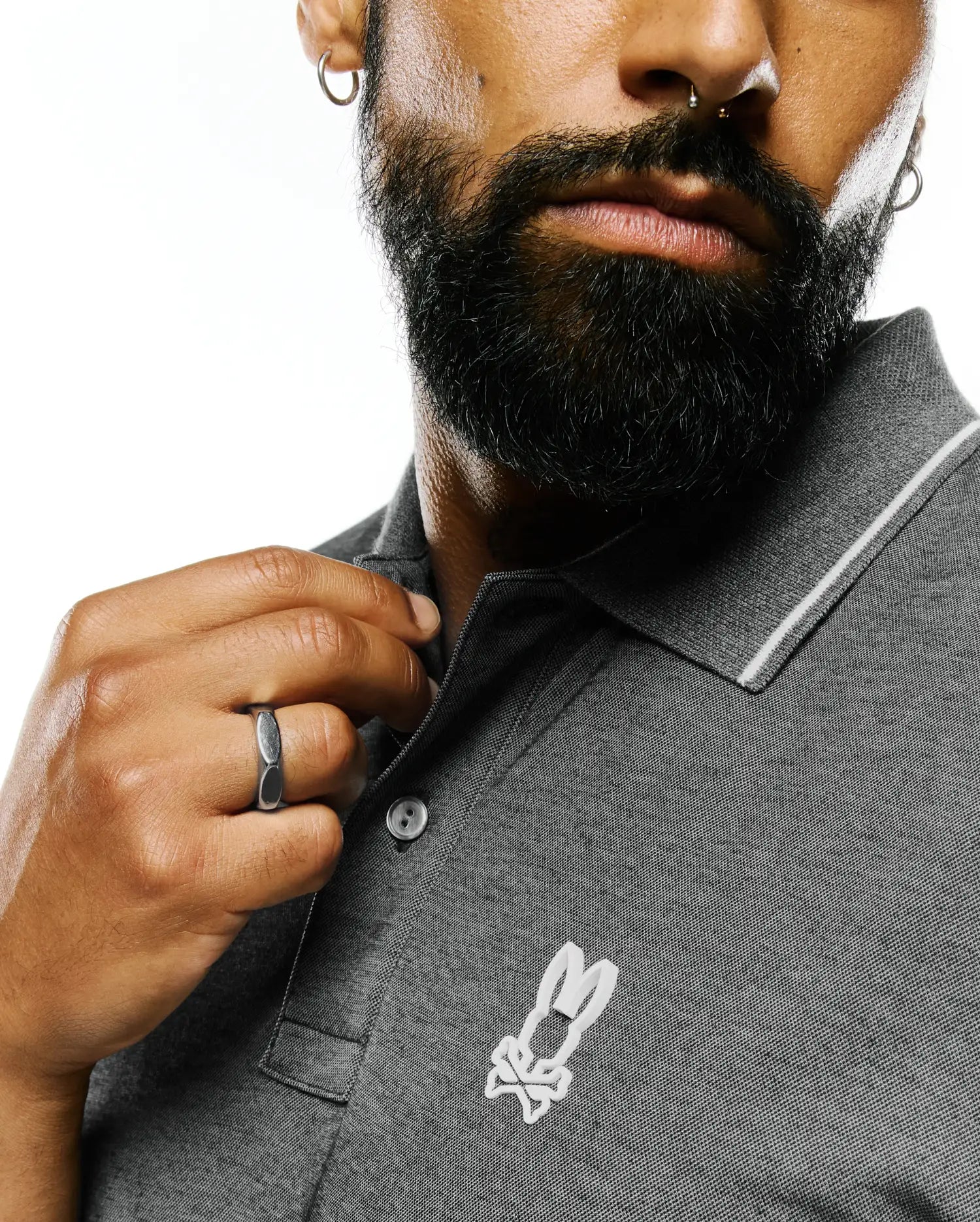 Mens Joji Performance Polo, a grey pique knit polo shirt featuring a classic fit, white tipping on the collar, a two-button placket, and a white embroidered Psycho Bunny skull logo on the left chest.
