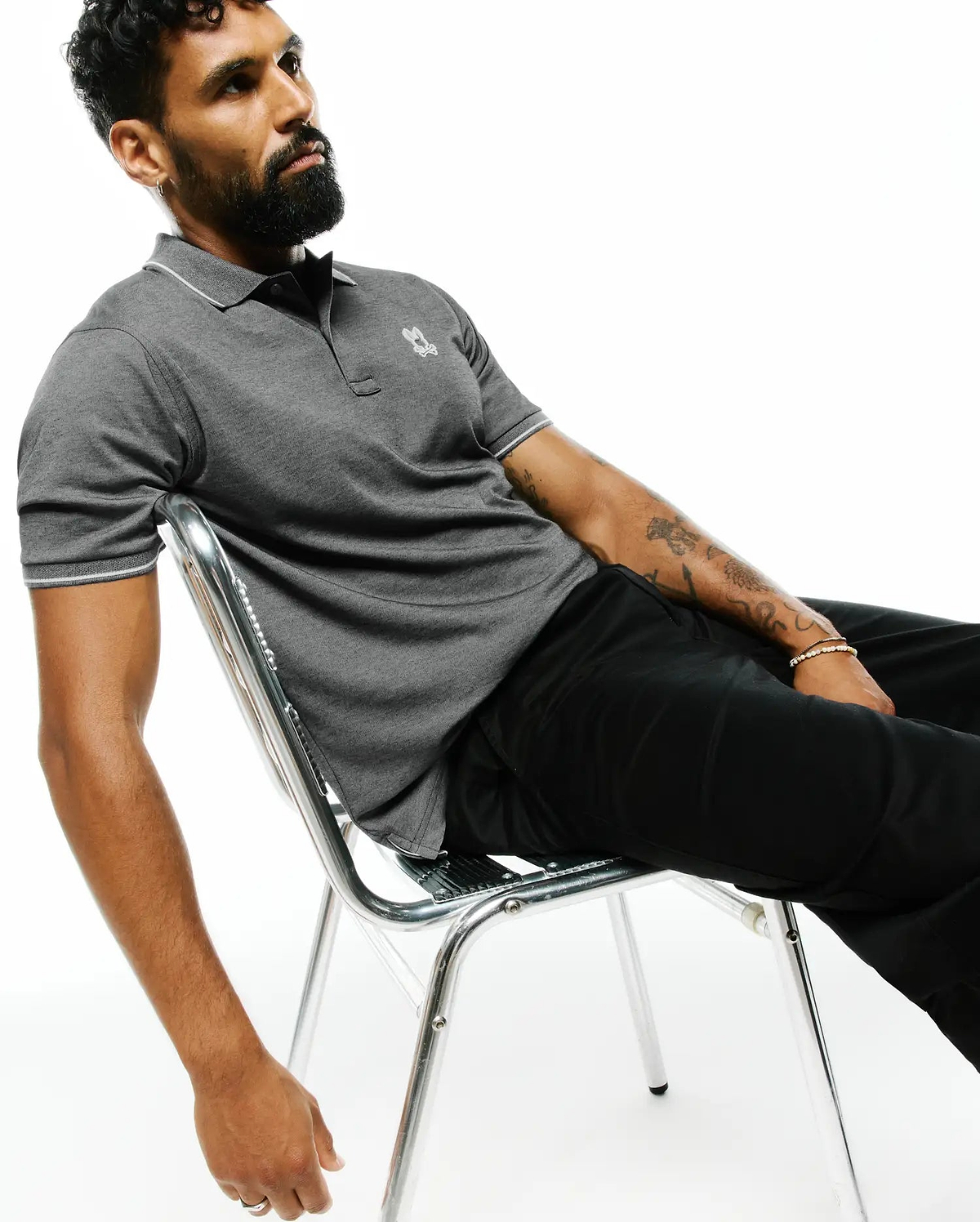 MENS JOJI PERFORMANCE POLO, a dark grey pique knit polo with a classic fit, white tipping on the collar and sleeve cuffs, and a small embroidered Psycho Bunny skull logo on the left chest.