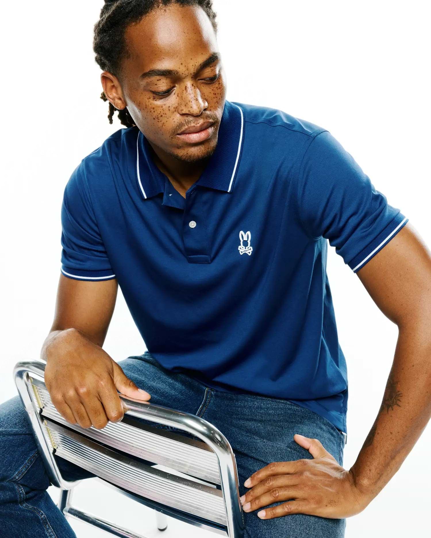 Men's Joji Performance Polo, a classic fit navy blue performance polo with white tipped collar and cuffs, featuring a small embroidered white Psycho Bunny skull logo on the left chest.