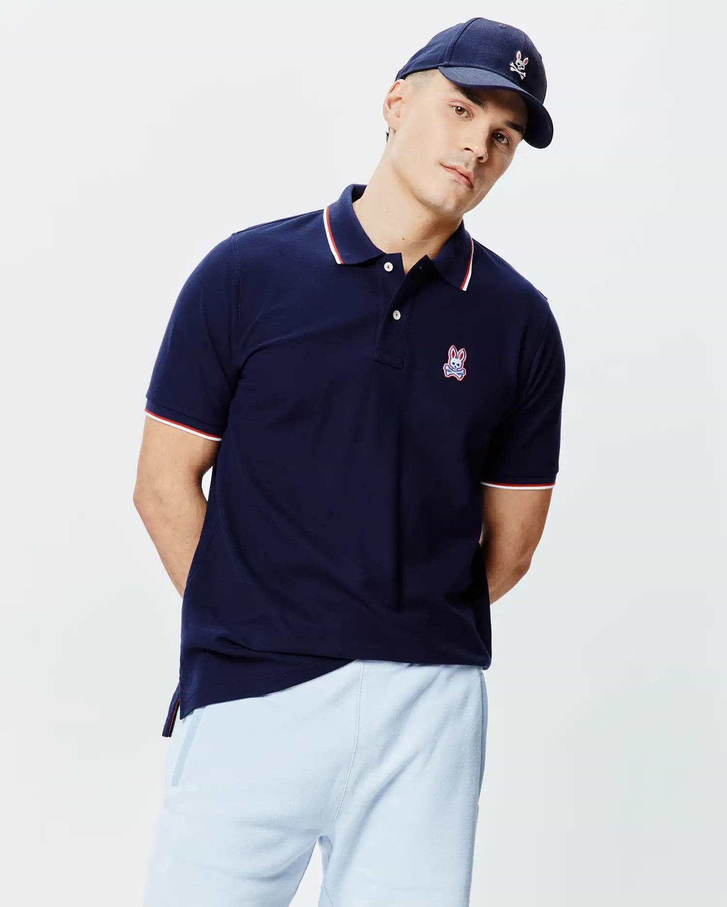 Navy blue Mens John Pique Polo, classic fit, with white two-button placket, ribbed collar and cuffs featuring red and white tipping, and an embroidered Psycho Bunny skull logo on the left chest.