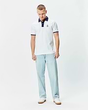 Mens John Pique Polo, a classic fit white pique polo with a navy collar, two-button placket, red and navy striped sleeve cuffs, and a small embroidered Psycho Bunny skull logo on the left chest.