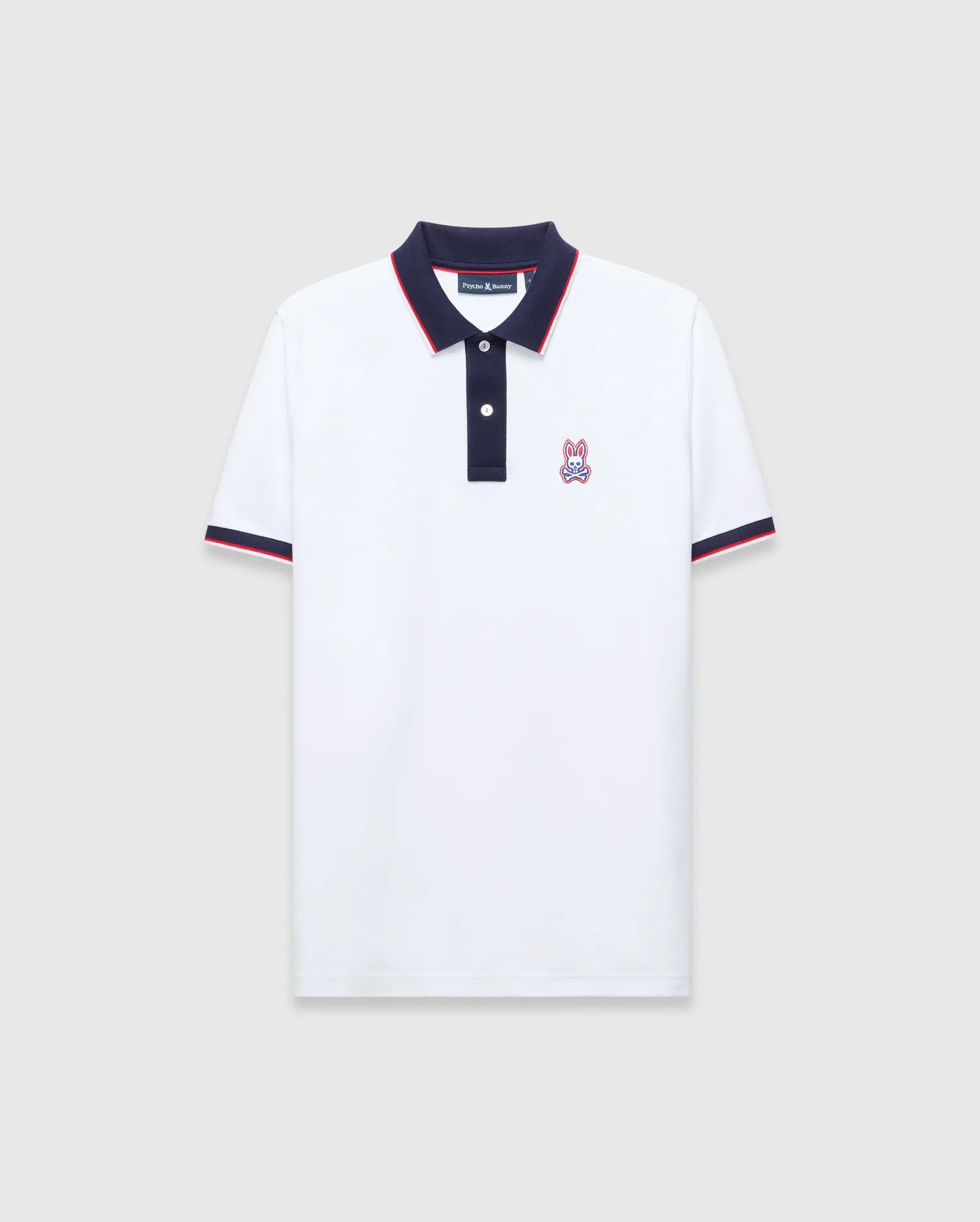 Mens John Pique Polo, a classic fit white pique polo with navy collar and placket, red tipping, navy ribbed cuffs with red stripe, and an embroidered Psycho Bunny skull logo on the left chest.