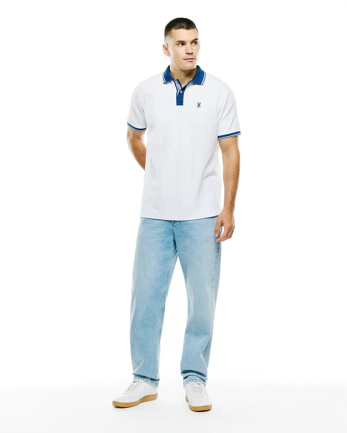 Mens Stan Pima Piqué Polo, a classic fit white polo with a royal blue collar, two-button placket, and striped cuffs, featuring a small embroidered Psycho Bunny skull logo on the left chest.
