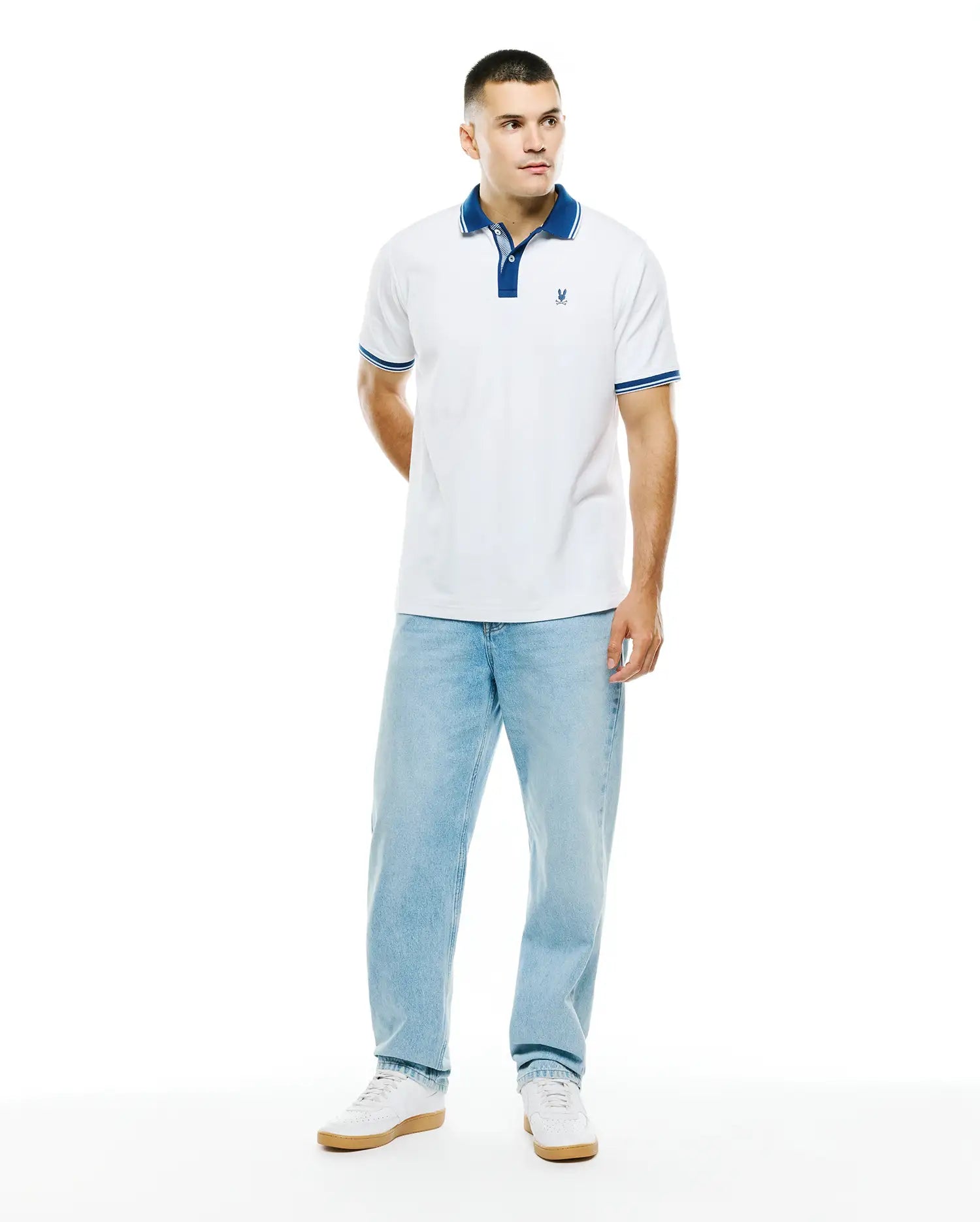 Mens Stan Pima Piqué Polo, a classic fit white polo with a royal blue collar, two-button placket, and striped cuffs, featuring a small embroidered Psycho Bunny skull logo on the left chest.
