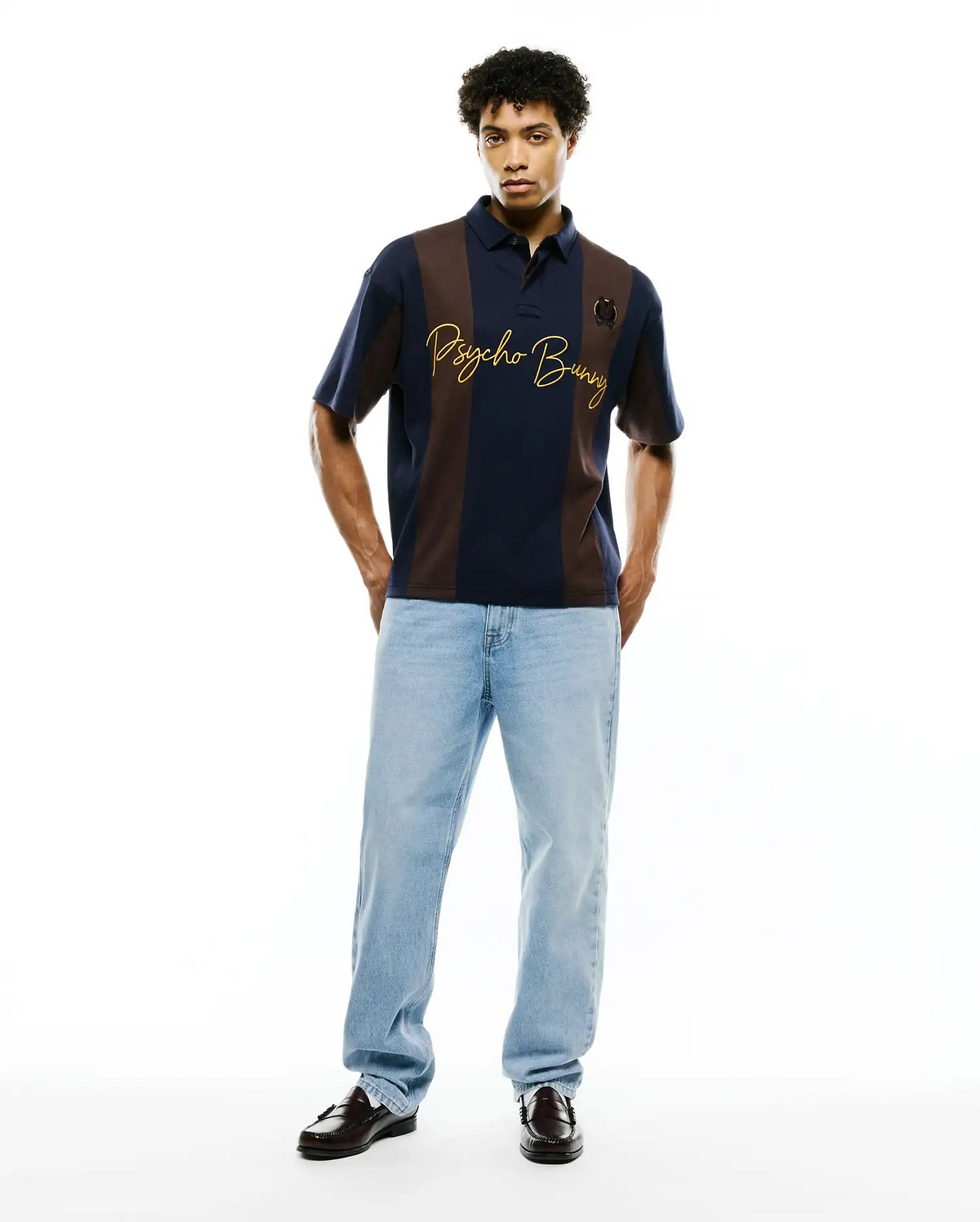 Mens Chad Relaxed Fit Striped Polo in navy blue and brown vertical stripes, featuring a jersey knit, large gold embroidered Psycho Bunny script, and a small circular emblem on the chest.