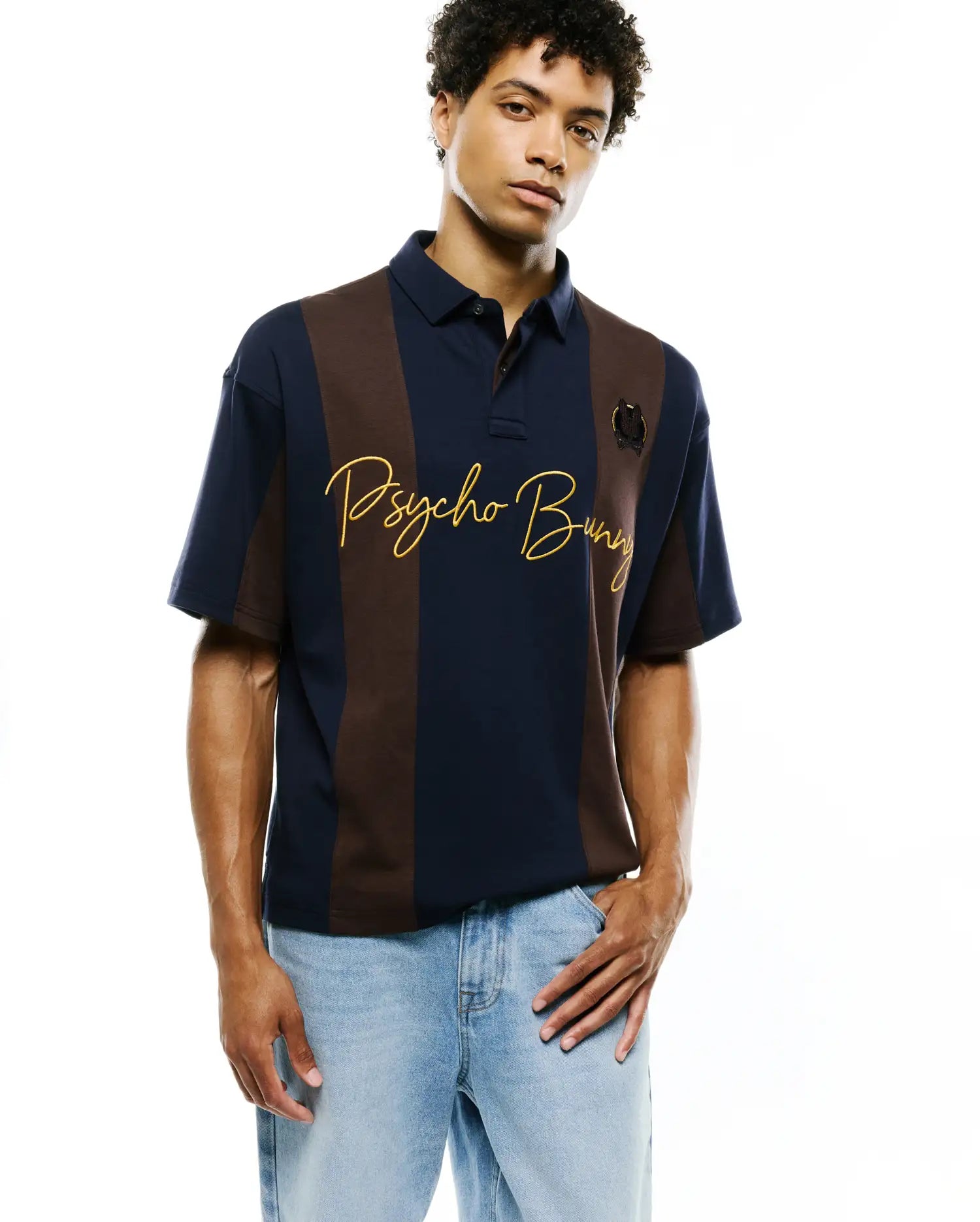 Mens Chad Relaxed Fit Striped Polo: Navy and brown vertical striped pique polo with gold embroidered Psycho Bunny script across the chest and a small embroidered bunny skull logo on the right chest.