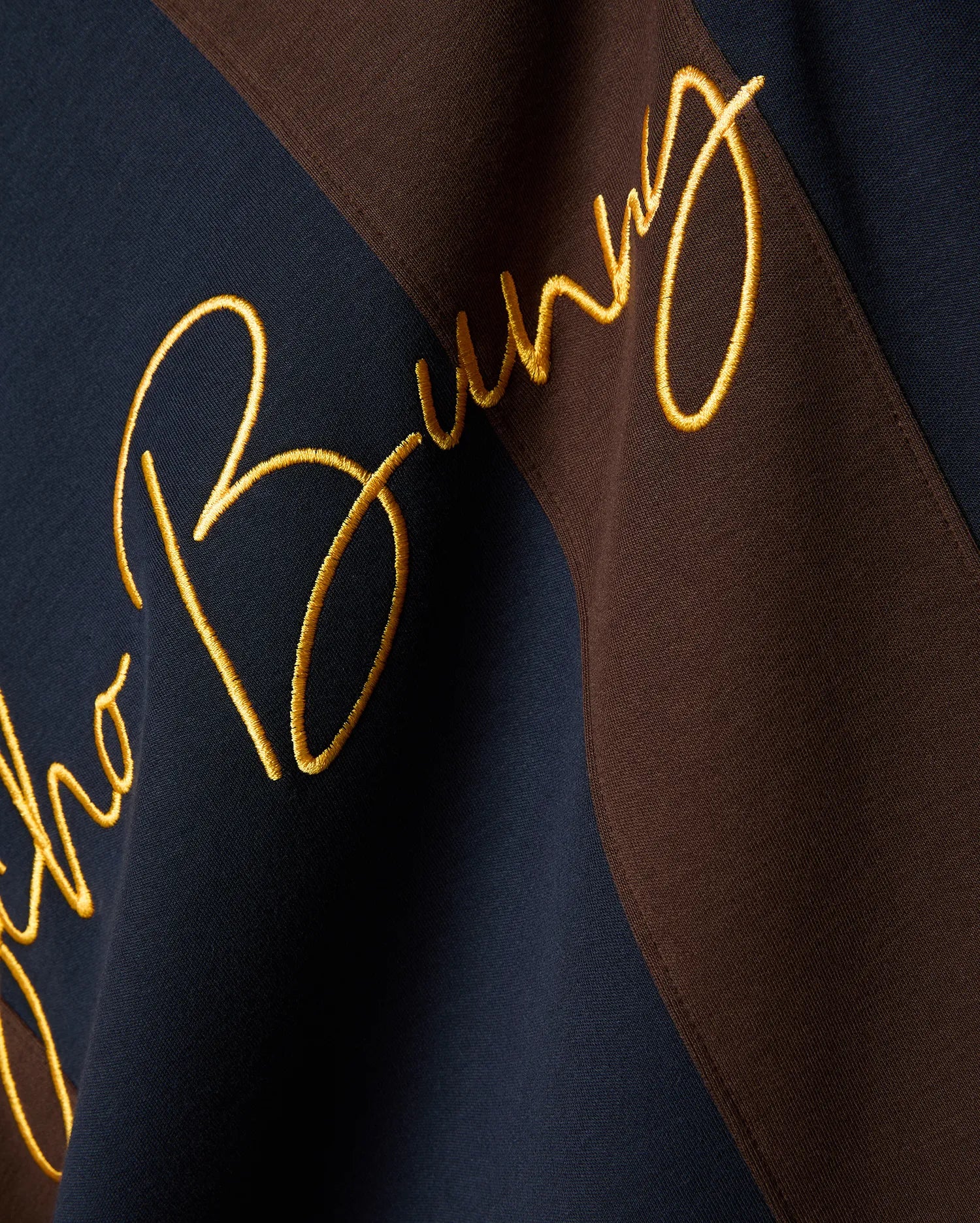 Mens Chad Relaxed Fit Striped Polo, a premium navy and brown diagonal striped pique polo featuring a large, central, gold embroidered Psycho Bunny script logo, embodying refined streetwear style.
