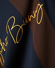 Mens Chad Relaxed Fit Striped Polo, a premium navy and brown diagonal striped pique polo featuring a large, central, gold embroidered Psycho Bunny script logo, embodying refined streetwear style.