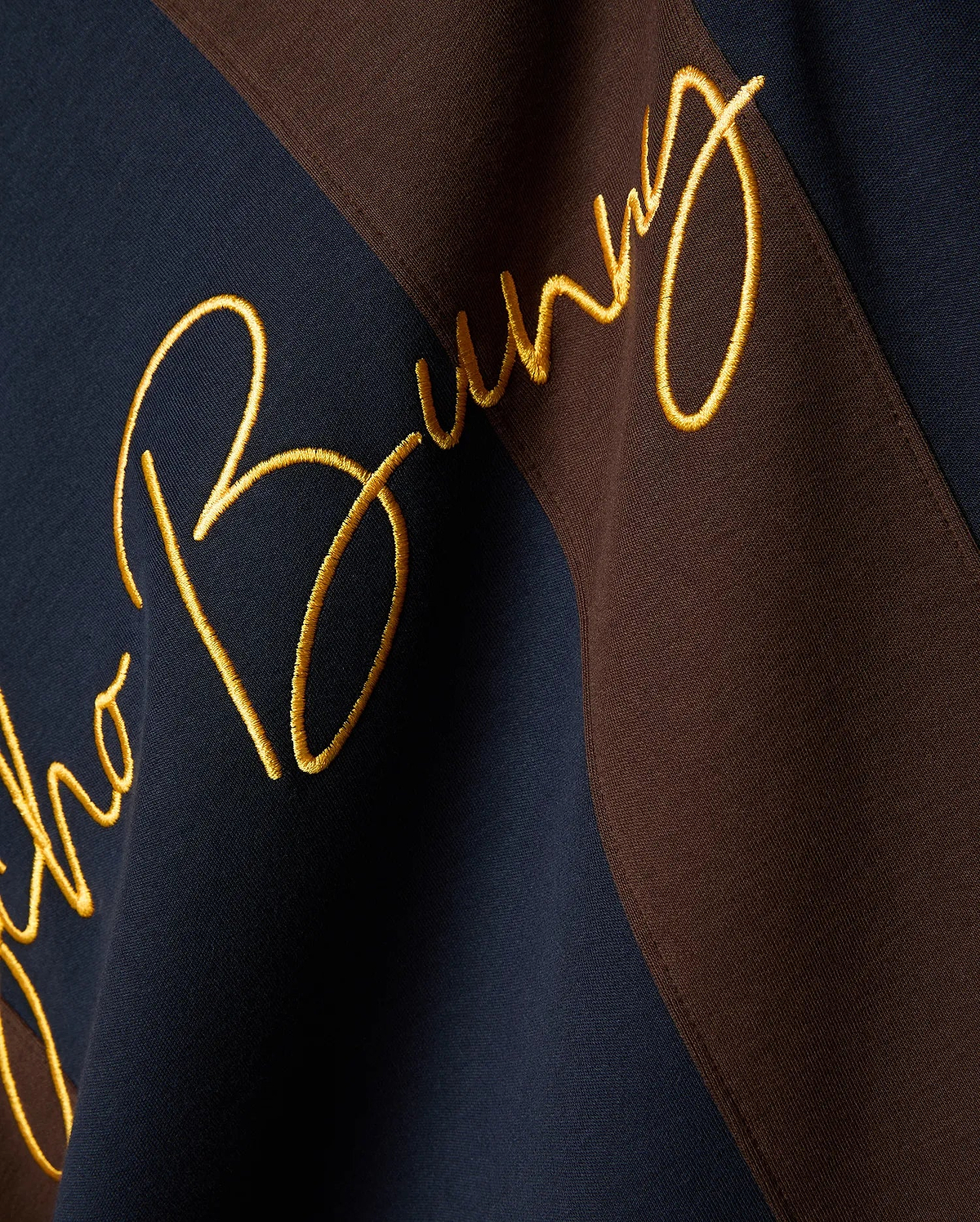 Mens Chad Relaxed Fit Striped Polo, a premium navy and brown diagonal striped pique polo featuring a large, central, gold embroidered Psycho Bunny script logo, embodying refined streetwear style.