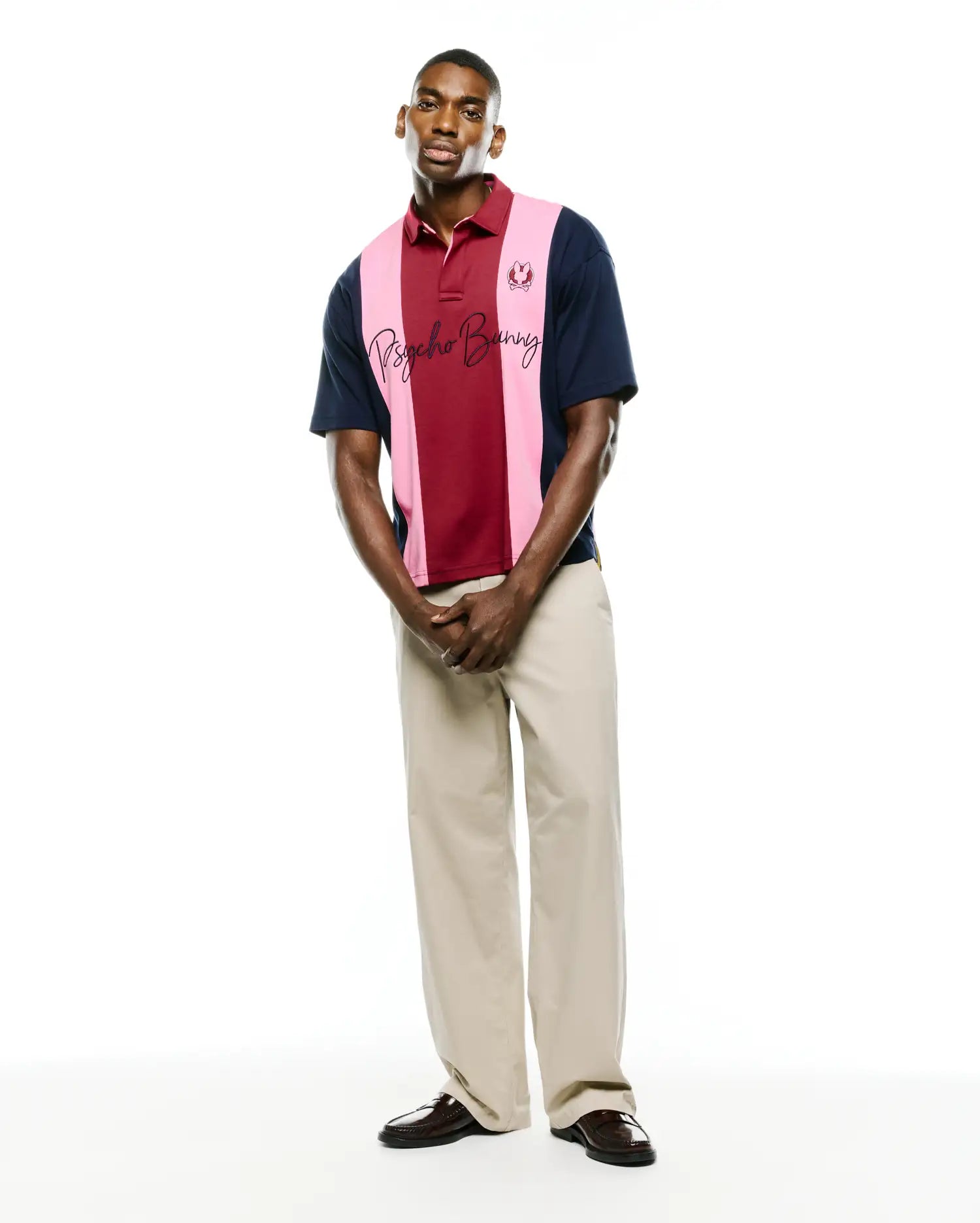 Mens Chad Relaxed Fit Striped Polo in navy, burgundy, and pink pique knit, featuring a small embroidered bunny skull on the left chest and a large script Psycho Bunny logo across the chest.