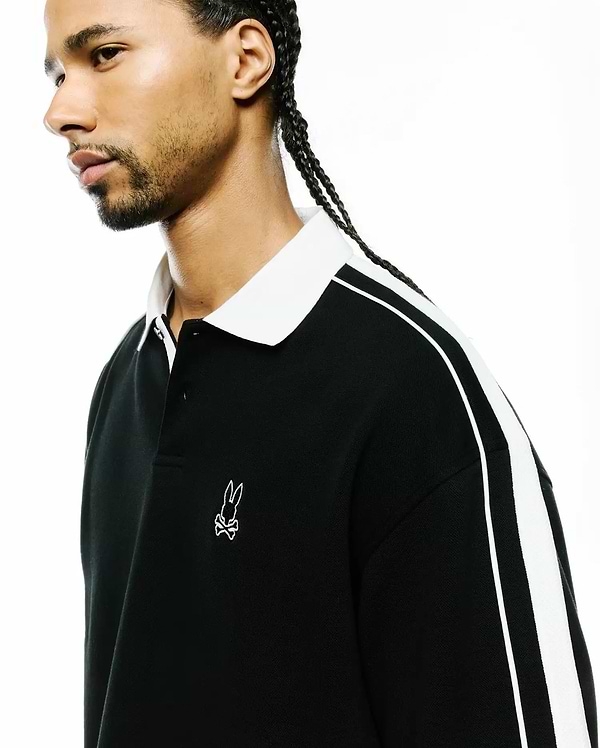 Mens Ceano Relaxed Fit Heavy Pique Polo in black with a crisp white collar, bold white double stripes on the sleeves, and a small white embroidered Psycho Bunny skull logo on the left chest.