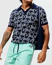 Mens Sidney Oversized Knit Polo, a navy short-sleeve polo with an all-over white Psycho Bunny skull logo pattern, featuring a textured knit fabric, solid navy collar, and cuffs.