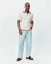 Mens Elowen Knit Polo in cream, featuring a ribbed texture, V-neck, and navy blue stripe accents on the collar, cuffs, and hem, with a small embroidered Psycho Bunny logo on the chest.