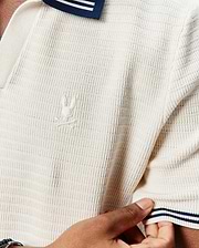 Mens Elowen Knit Polo in cream, featuring a textured knit fabric, classic fit, navy and white striped collar and sleeve cuffs, and a small embroidered Psycho Bunny skull logo on the left chest.
