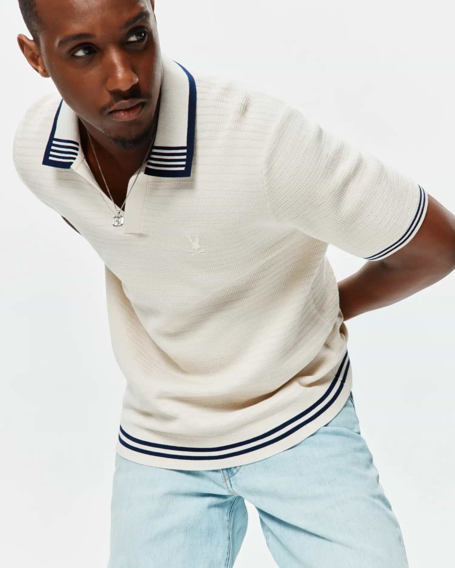 Mens Elowen Knit Polo in cream, featuring a ribbed knit texture, navy and white striped collar, cuffs, and hem, with a small embroidered Psycho Bunny skull logo on the left chest.
