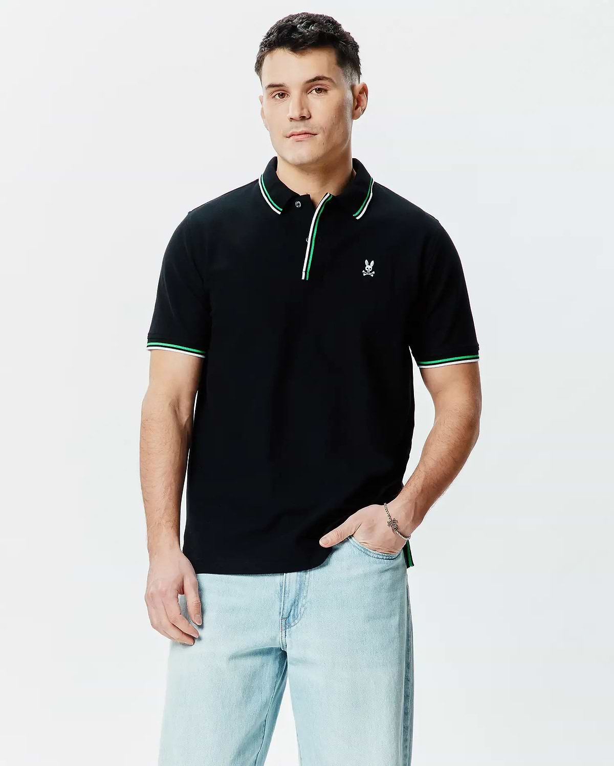 Mens Faye Pique Polo, a classic fit black pique polo shirt with a small embroidered white Psycho Bunny skull logo on the left chest, featuring green and white tipping on the collar and sleeve cuffs.