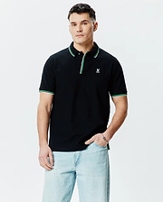 Mens Faye Pique Polo, a classic fit black pique polo shirt with a small embroidered white Psycho Bunny skull logo on the left chest, featuring green and white tipping on the collar and sleeve cuffs.
