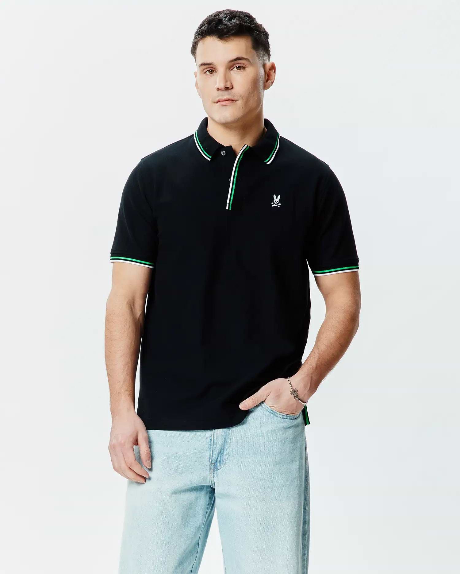 Mens Faye Pique Polo, a classic fit black pique polo shirt with a small embroidered white Psycho Bunny skull logo on the left chest, featuring green and white tipping on the collar and sleeve cuffs.