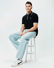 Mens Faye Pique Polo, black classic fit with pique texture, featuring green and white striped collar and cuffs, and a small embroidered Psycho Bunny skull logo on the left chest.