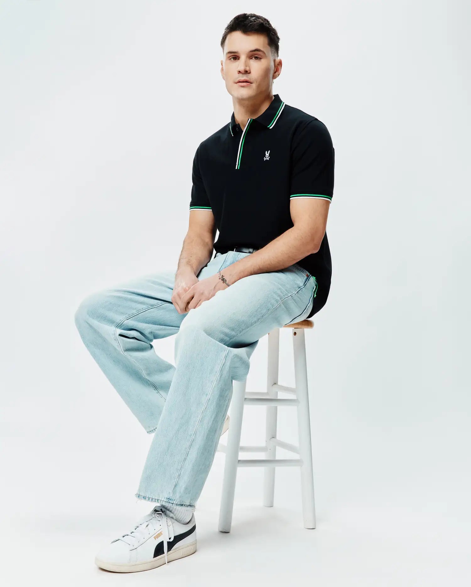Mens Faye Pique Polo, black classic fit with pique texture, featuring green and white striped collar and cuffs, and a small embroidered Psycho Bunny skull logo on the left chest.