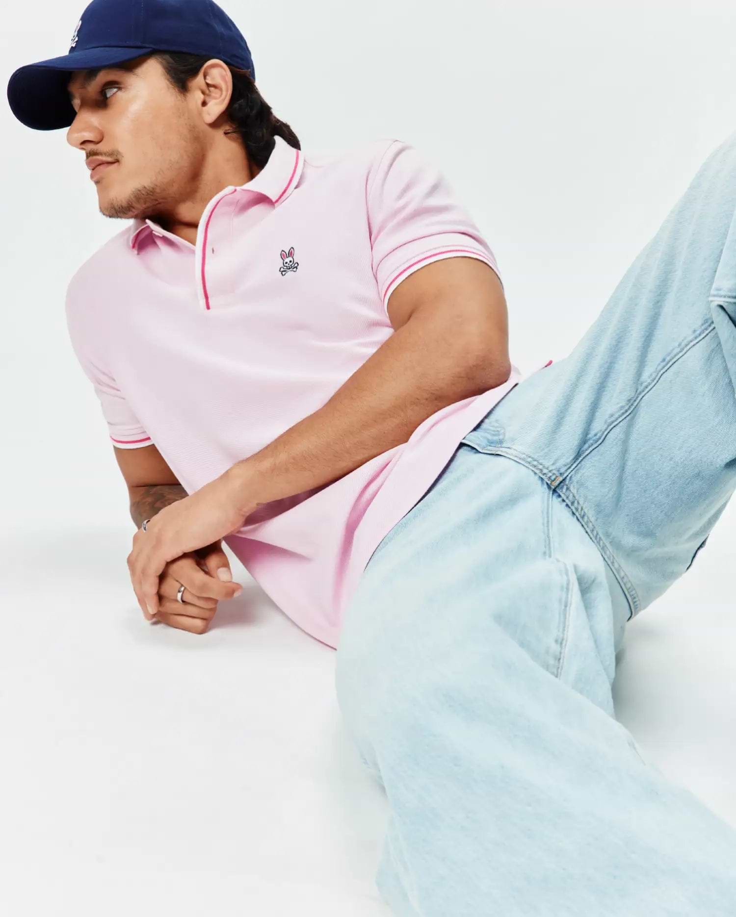 Mens Faye Pique Polo in light pink, a classic fit with textured pique fabric, featuring a small embroidered Psycho Bunny skull logo on the left chest and vibrant red striped trim on the collar and sleeve cuffs.