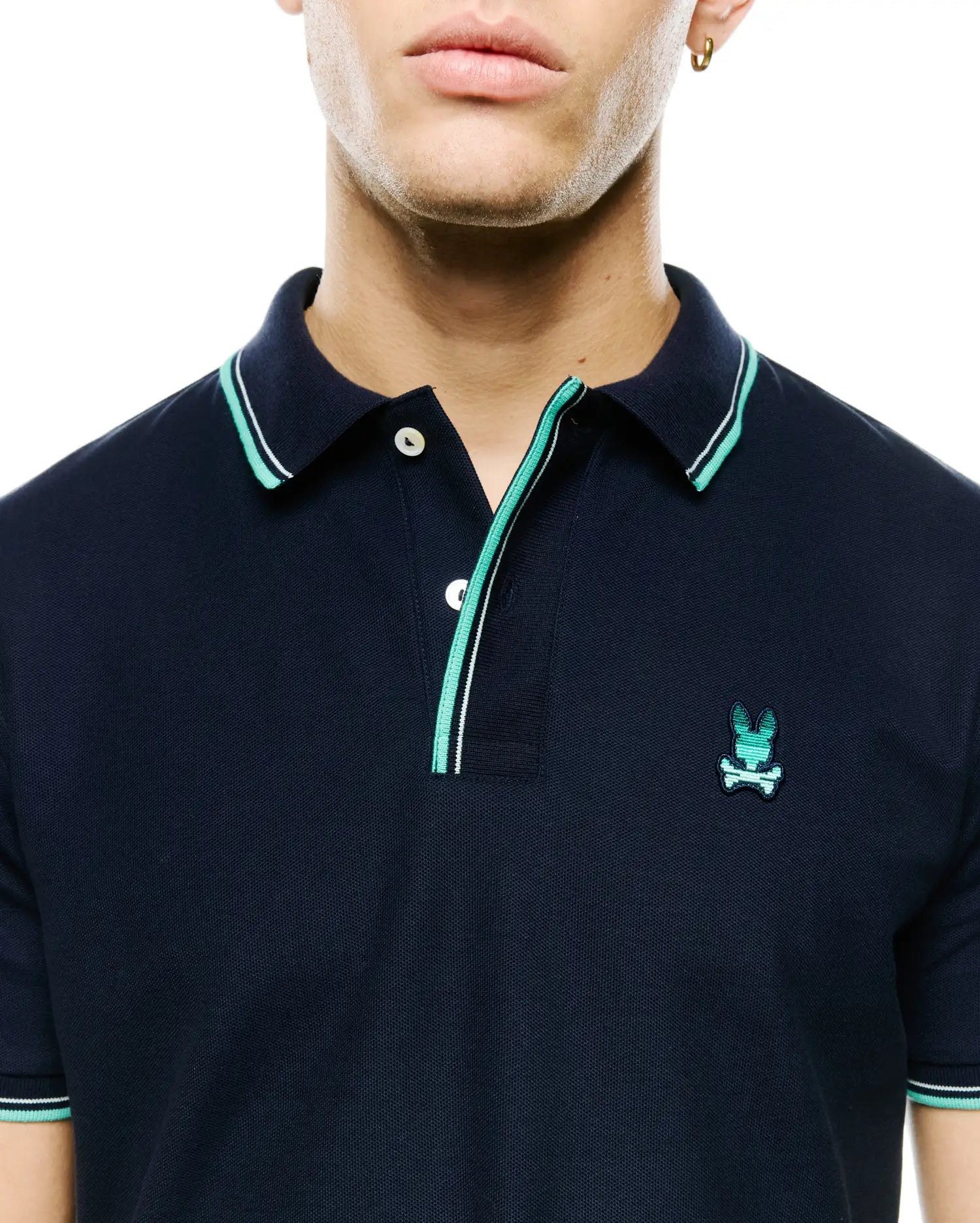 Men's Slade Pique Polo, a navy classic fit pique polo with teal and white tipped collar and cuffs, two-button placket, and small embroidered teal Psycho Bunny skull logo on left chest. (2)