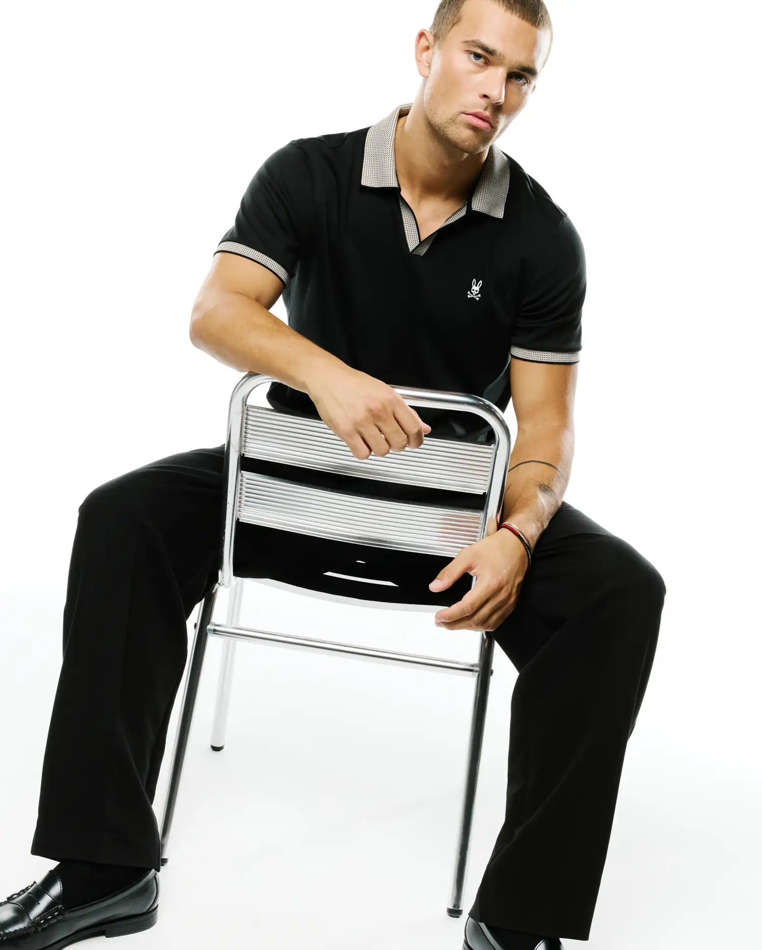 Men's Teddy Johnny Collar Polo, black pique knit with a classic fit, featuring a contrasting light grey patterned Johnny collar and sleeve cuffs, and a small white embroidered Psycho Bunny skull logo on the left chest. (3)