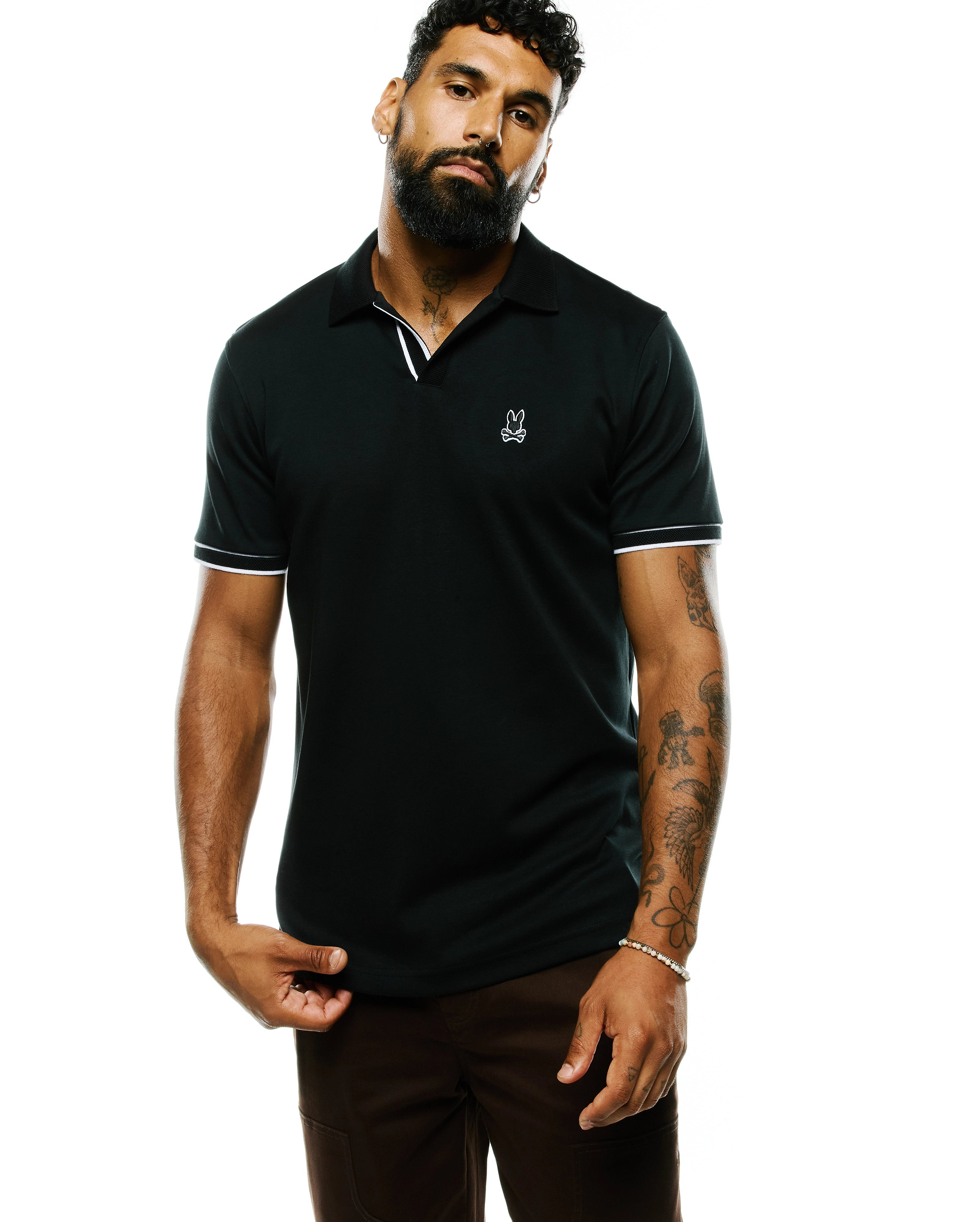 Mens Nasser Pima Johnny Polo, a dark green classic fit pima cotton polo with white tipping on the ribbed collar and cuffs, featuring a small white embroidered Psycho Bunny skull logo on the left chest.