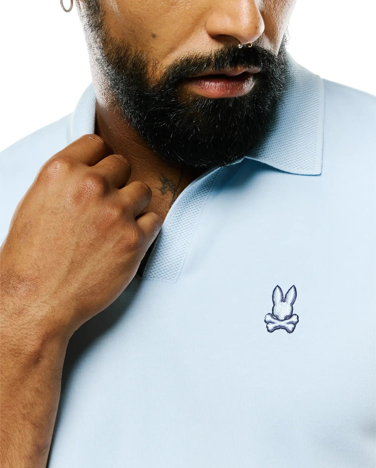 Mens Nasser Pima Johnny Polo in light blue Pima cotton jersey with a classic fit, featuring a textured pique collar and a small embroidered white and navy Psycho Bunny skull logo on the left chest.