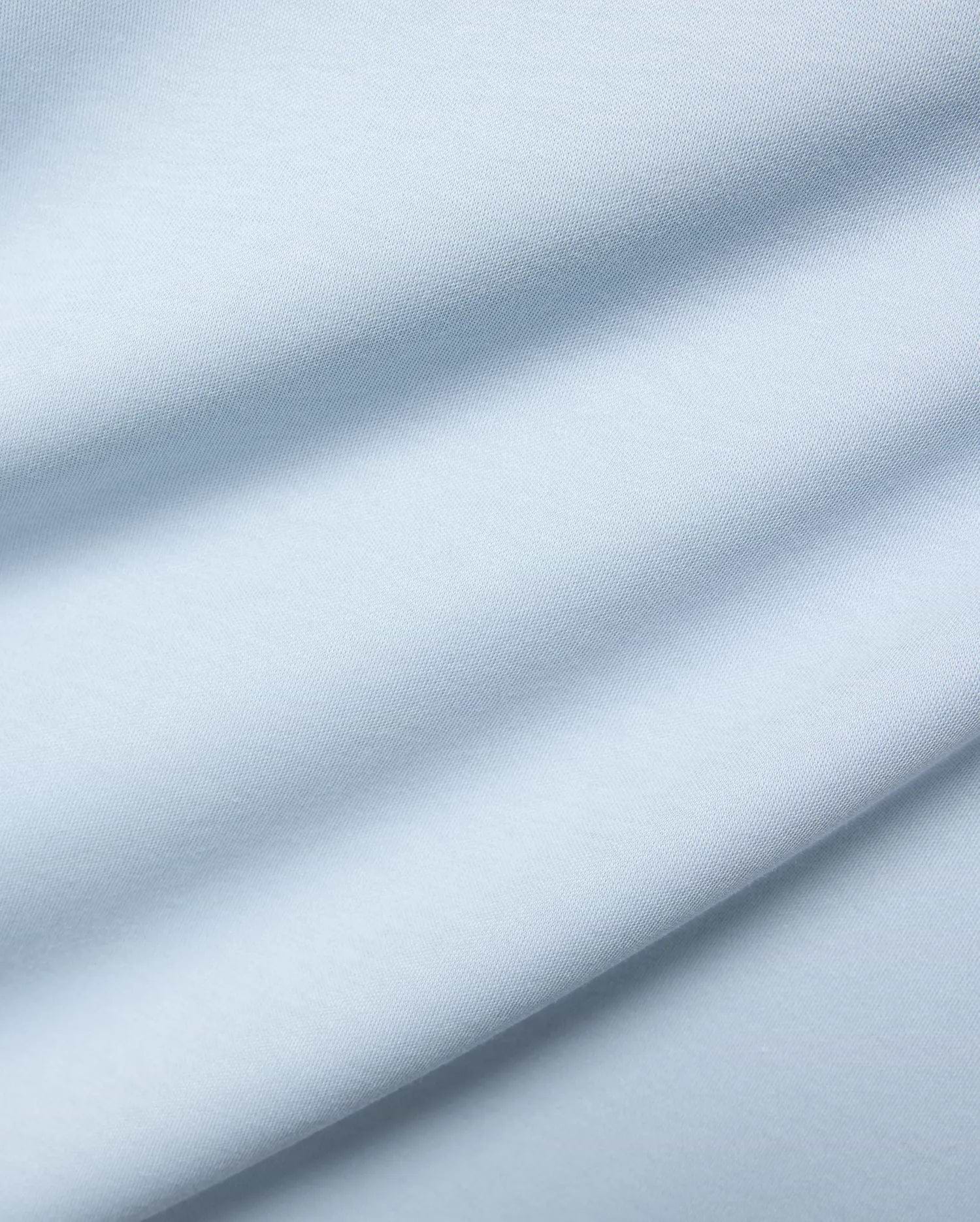 Mens Nasser Interlock Johnny Collar Polo, featuring a close-up of its soft, light blue interlock knit fabric with subtle texture and elegant draped folds.