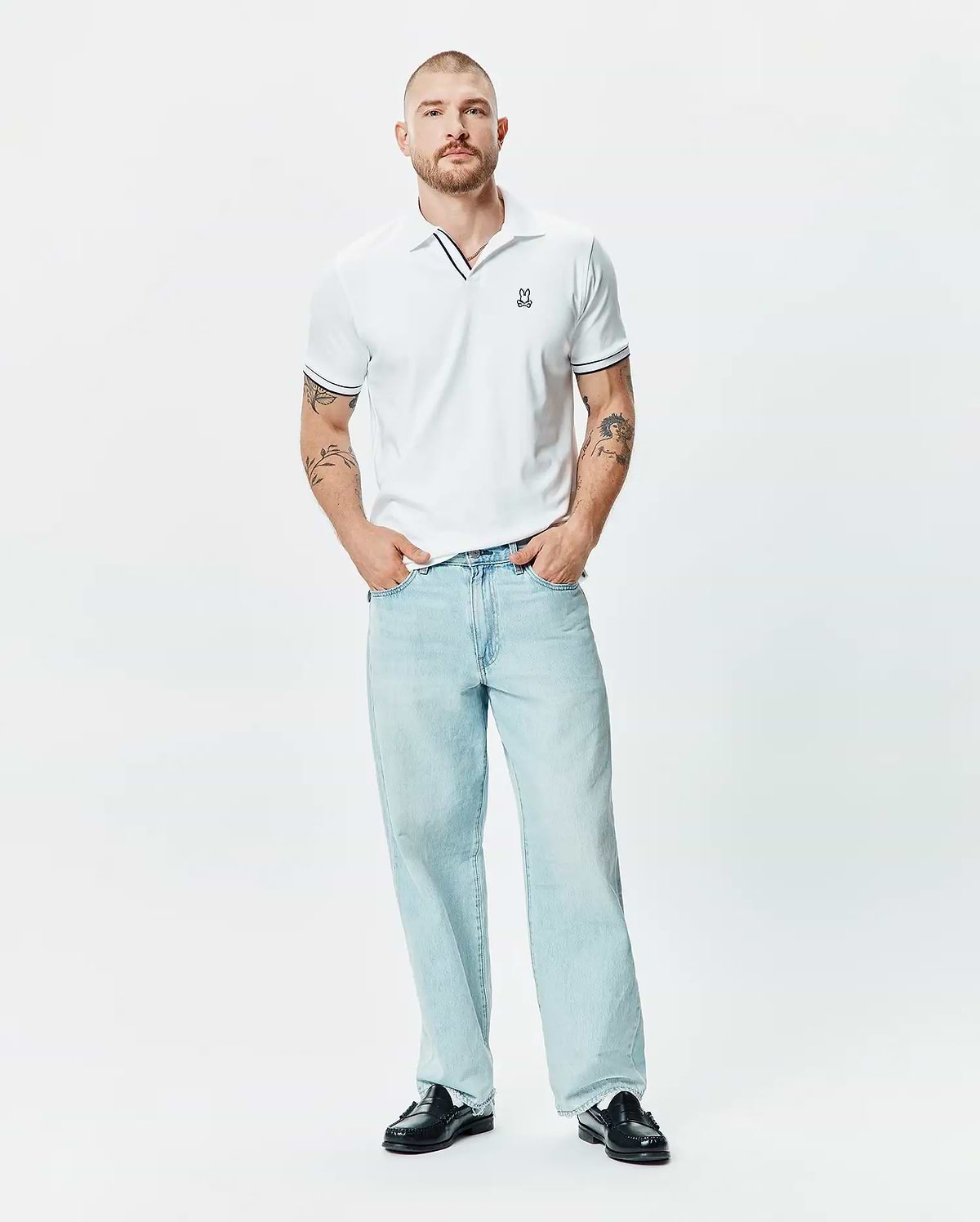 Mens Nasser Polo, a classic fit white pique polo with black tipping on the collar and sleeve cuffs, featuring a small embroidered Psycho Bunny skull logo on the left chest.