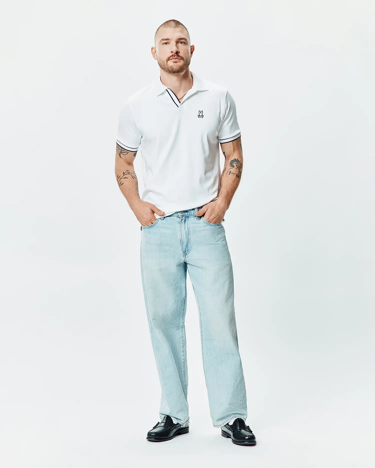 Mens Nasser Polo, a classic fit white pique polo with black tipping on the collar and sleeve cuffs, featuring a small embroidered Psycho Bunny skull logo on the left chest.
