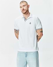 Mens Nasser Polo, white pique knit, classic fit, with navy blue striped collar and cuffs, featuring a small embroidered Psycho Bunny skull logo on the left chest.