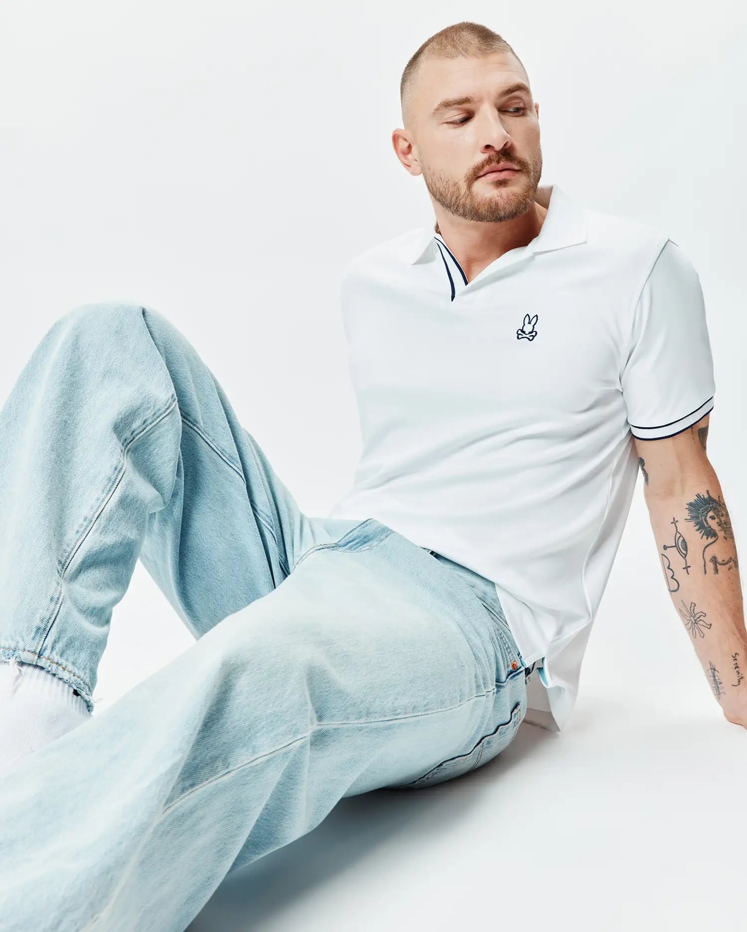 White Mens Nasser Polo in classic pique knit, featuring navy blue striped collar and cuffs, with a small embroidered Psycho Bunny skull logo on the left chest.