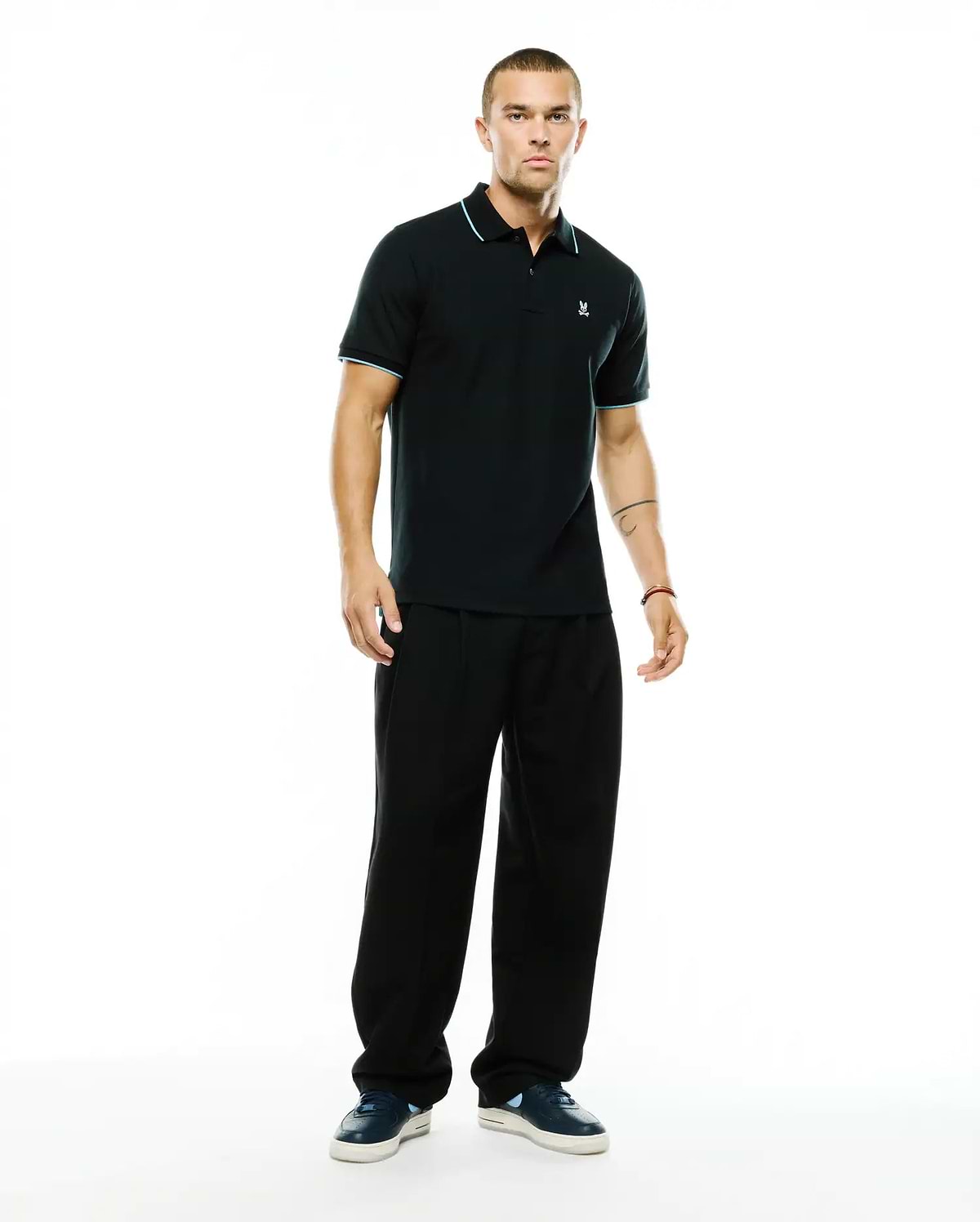 Men's Klaus Pique Polo, a classic fit black pique polo with light blue tipping on the collar and sleeve cuffs, featuring a small embroidered Psycho Bunny skull logo on the left chest. (4)