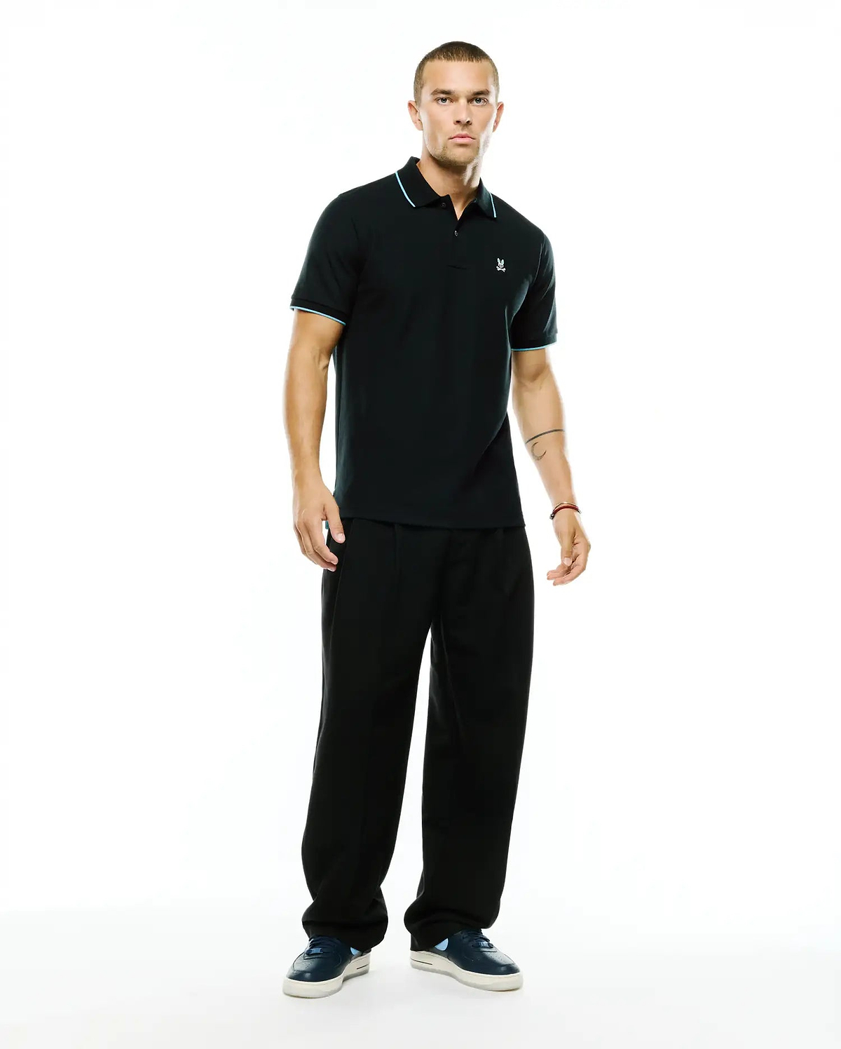 Men's Klaus Pique Polo, a classic fit black pique polo with light blue tipping on the collar and sleeve cuffs, featuring a small embroidered Psycho Bunny skull logo on the left chest. (4)