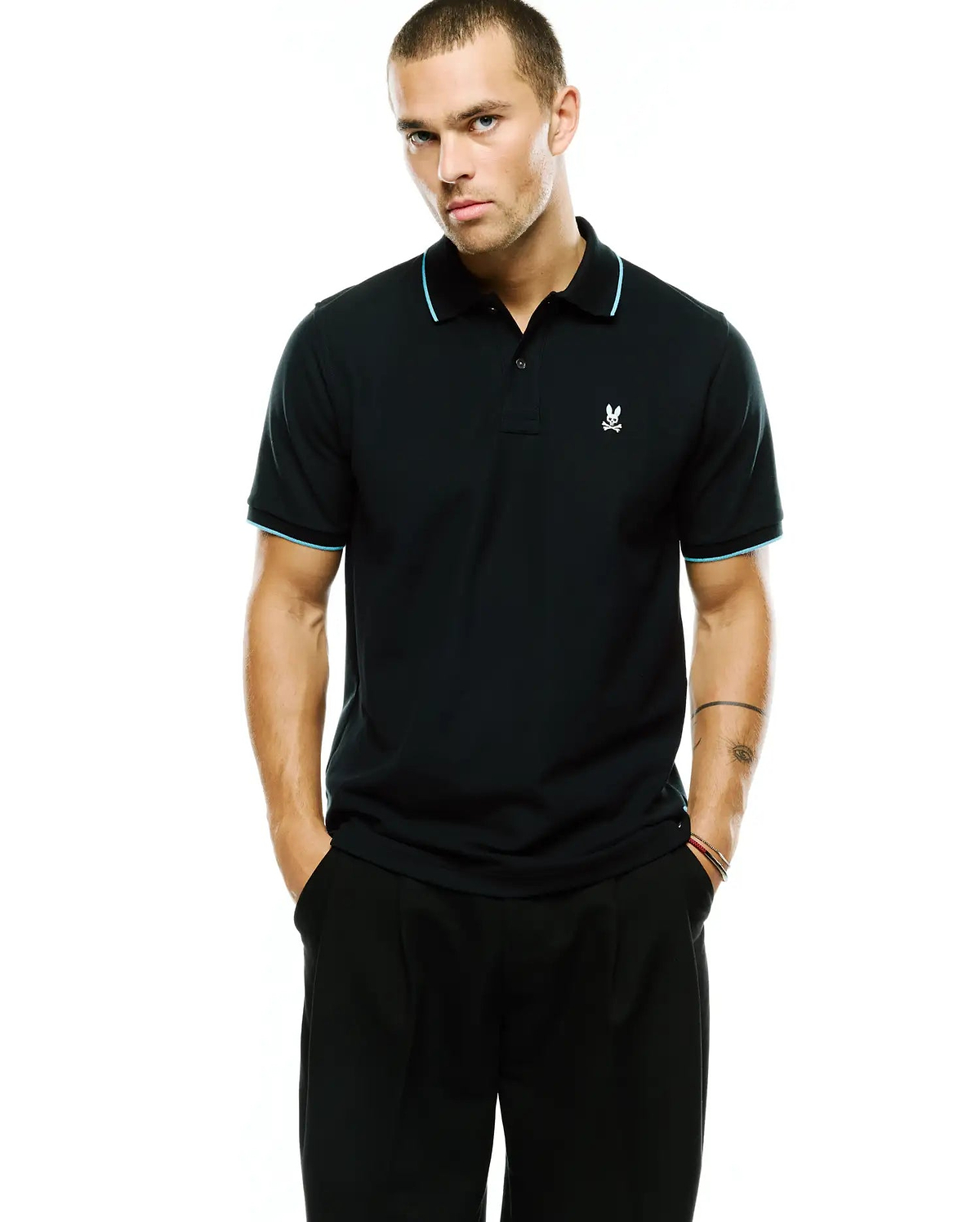 Men's Klaus Pique Polo, a classic fit black pique polo with light blue tipping on the ribbed collar and cuffs, featuring a small embroidered white Psycho Bunny skull logo on the left chest. (1)