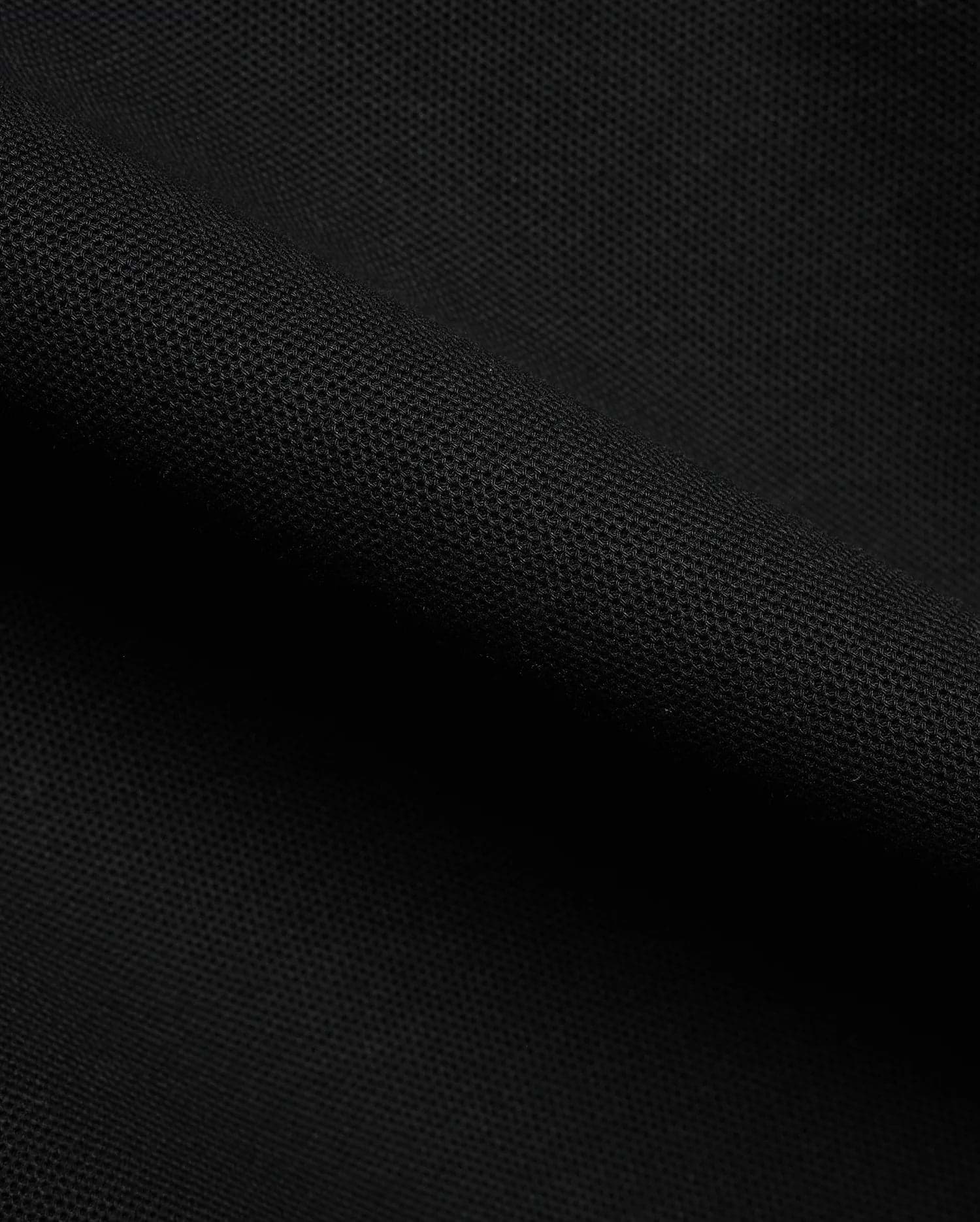 Detailed close-up of a rich black pique fabric, revealing the distinctive textured weave of the premium Men's Klaus Pique Polo, a signature Psycho Bunny menswear piece. (6)