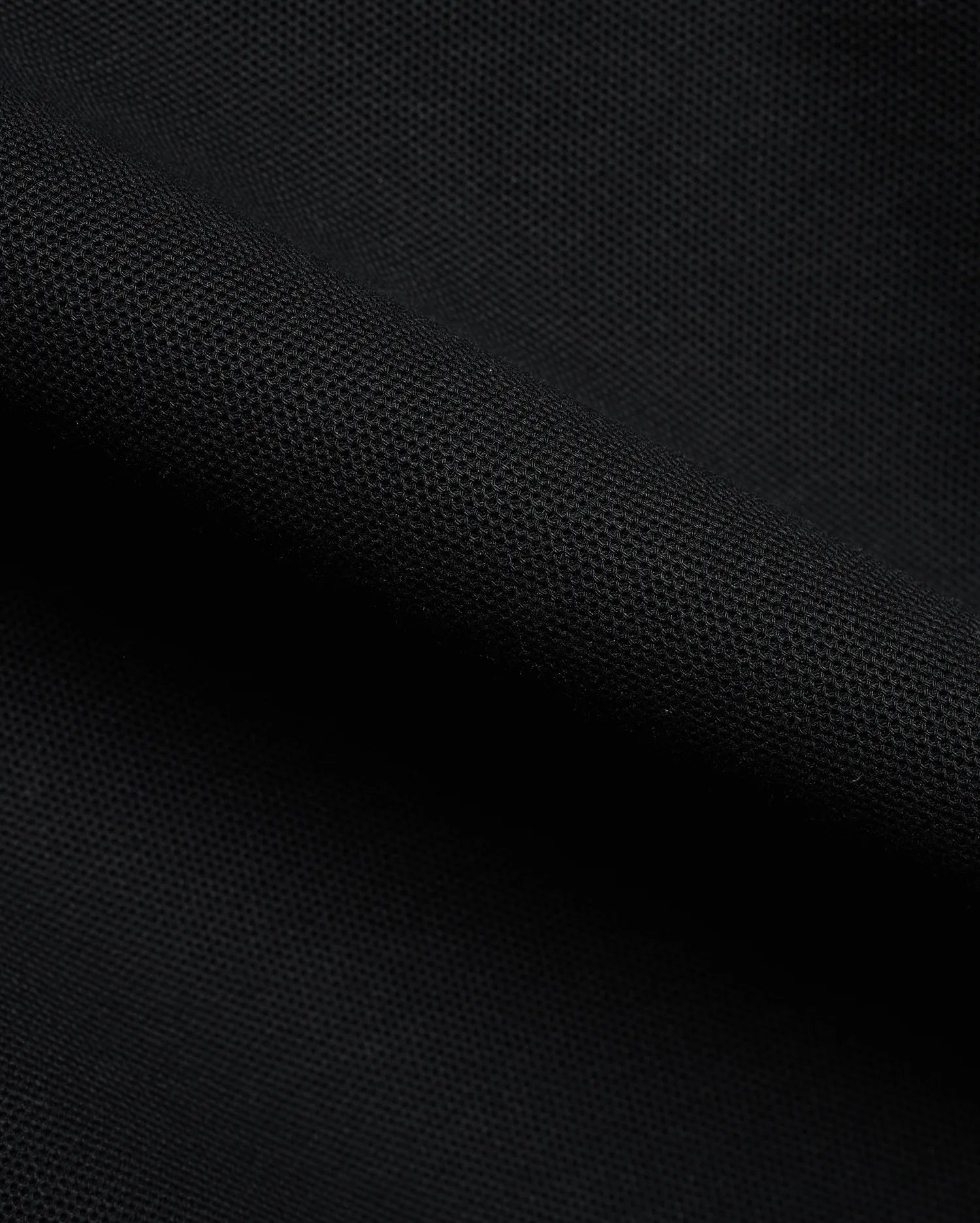Detailed close-up of a rich black pique fabric, revealing the distinctive textured weave of the premium Men's Klaus Pique Polo, a signature Psycho Bunny menswear piece. (6)