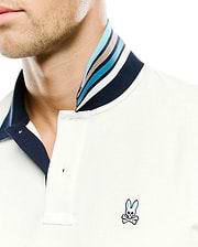 Men's Klaus Pique Polo in cream, featuring a classic fit, two-button placket, and a navy blue collar with multi-colored stripes in blues, white, and tan. The small, embroidered Psycho Bunny skull logo with blue ears is on the left chest. (2)